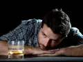 Mężczyzna zamyślony nad szklanką alkoholu. Może to być symbol walki z nałogiem, gdzie aplikacja "jestem wolny od" mogłaby pomóc.