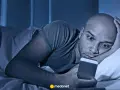 Mężczyzna leży w łóżku, wpatrując się w telefon. Czy to już obsesja?