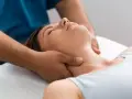 Fizjoterapeuta delikatnie masuje szyję kobiety, łagodząc napięcie. To jak ulga, gdy znika uczucie włosów w gardle.