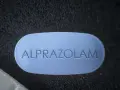 Niebieska tabletka z napisem "ALPRAZOLAM" leży obok białej. Uważaj na niebezpieczne skutki połączenia xanax i alkohol.