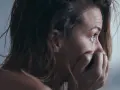 Kobieta zamyka usta dłonią, jej oczy wyrażają niepokój. Czy to początek hikikomori?
