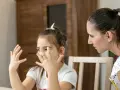 Dziewczynka z rękami przed twarzą, jakby przechodziła parentyfikację test. Kobieta patrzy na nią z uwagą.