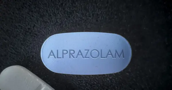 Niebieska tabletka z napisem "ALPRAZOLAM" leży obok białej. Uważaj na niebezpieczne skutki połączenia xanax i alkohol.