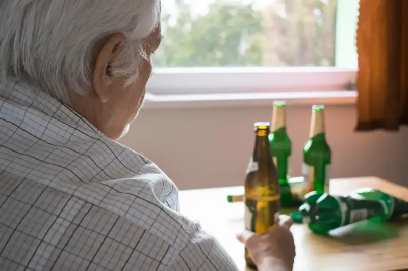 Starszy mężczyzna z butelkami piwa. Alkoholizm po 70. to trudna walka.