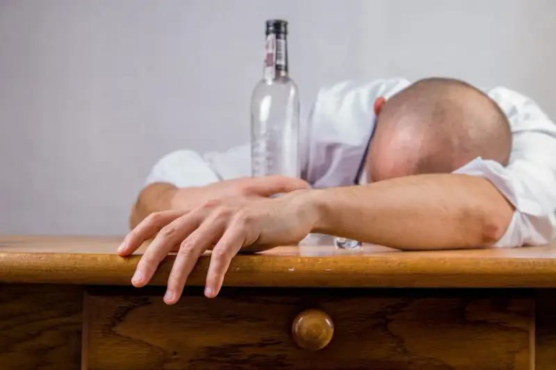 Mężczyzna śpi na stole, obok pusta butelka. Połączenie kofeiny i alkoholu doprowadziło do wyczerpania.